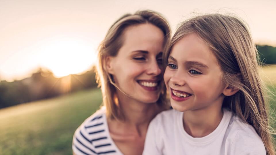 A mother and her daughter outside on a sunny evening smiling together